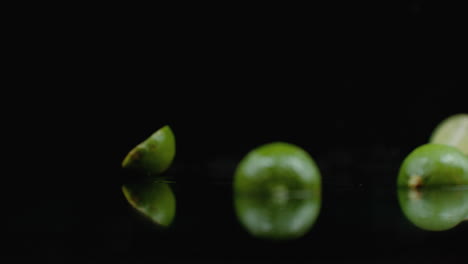 Two-ripe-cut-green-limes-fall-on-glass-with-splashes-of-water-in-slow-motion-on-a-dark-background